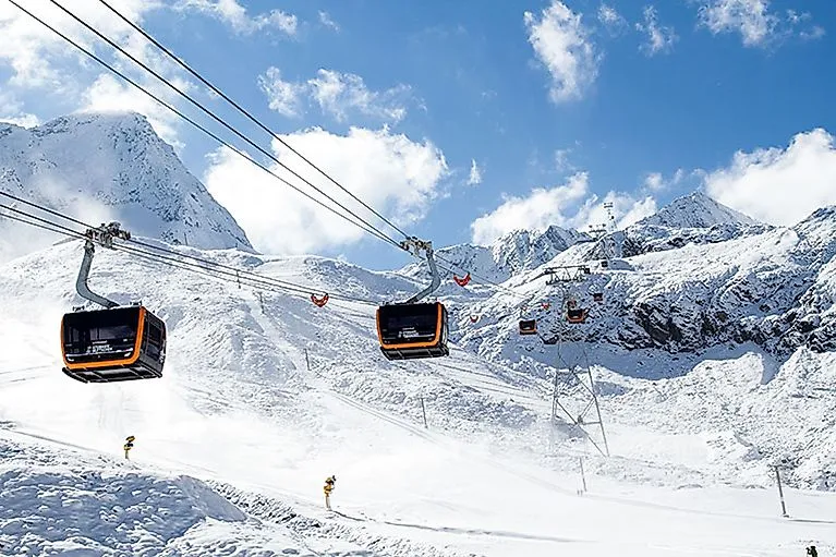 The modern 3S ice ridge lift travels through the snow-covered mountain landscape of the Stubai Glacier under a blue sky.