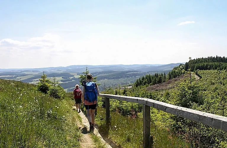 Two hikers on a path near Winterberg in the Sauerland with a wide view over green hills and forests on a summer's day