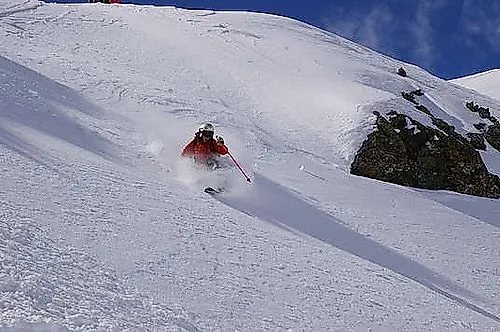 Sciatore con una giacca rossa che scia nella neve fresca e profonda su una pista di Livigno in un clima invernale splendido