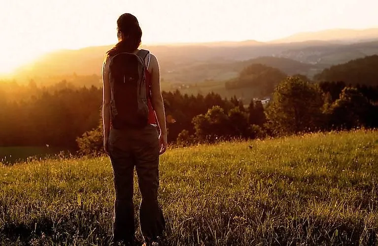 Woman with rucksack looks out over the Ilz valley and the hills at sunset