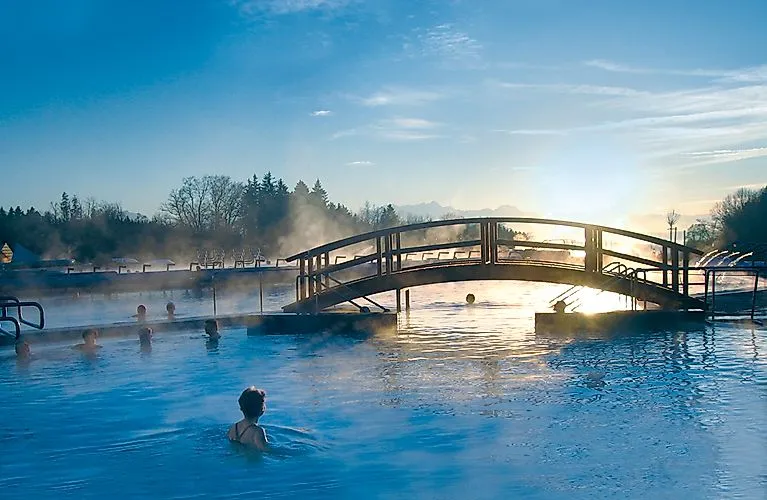 Al atardecer, la gente disfruta del agua caliente de los baños termales de Chiemgau, en Bad Endorf, con vistas a las montañas.