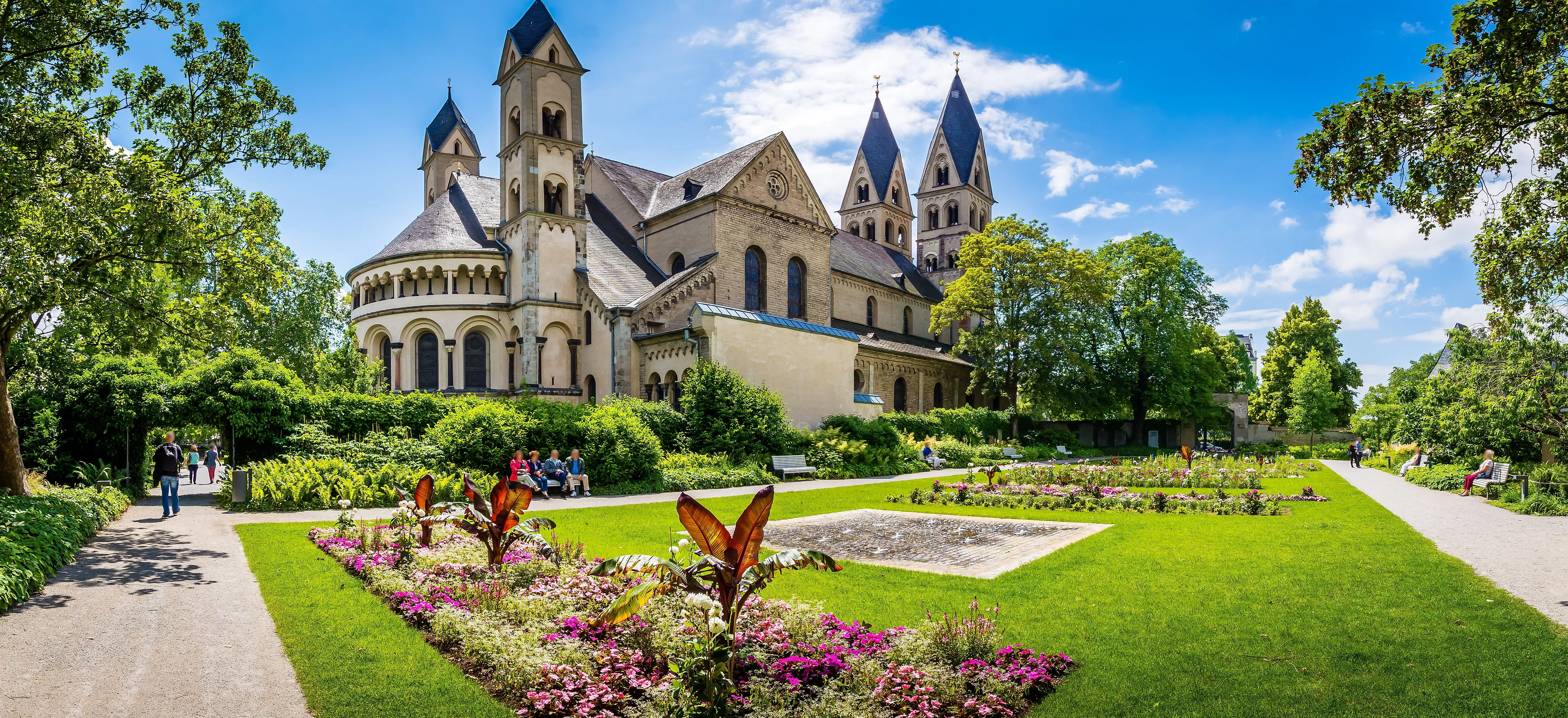 Romanesque Basilica of St. Castor in Koblenz with well-tended gardens on a sunny day.