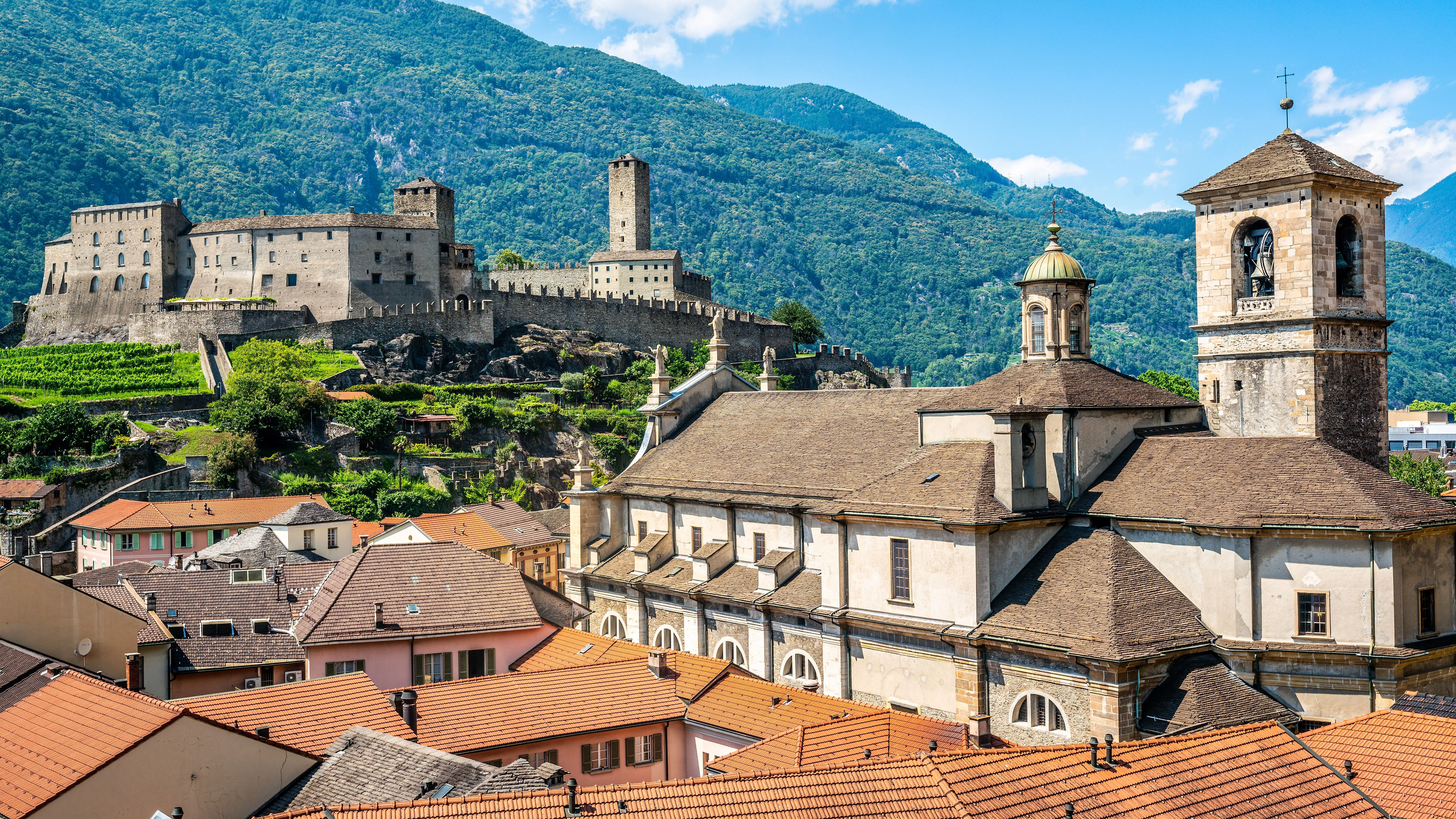 Historický hrad Castelgrande ve švýcarské Bellinzoně na pozadí zelených hor a červených taškových střech