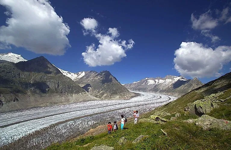 Wanderer auf einem Panoramaweg mit Blick auf den beeindruckenden Aletschgletscher in den Schweizer Alpen.