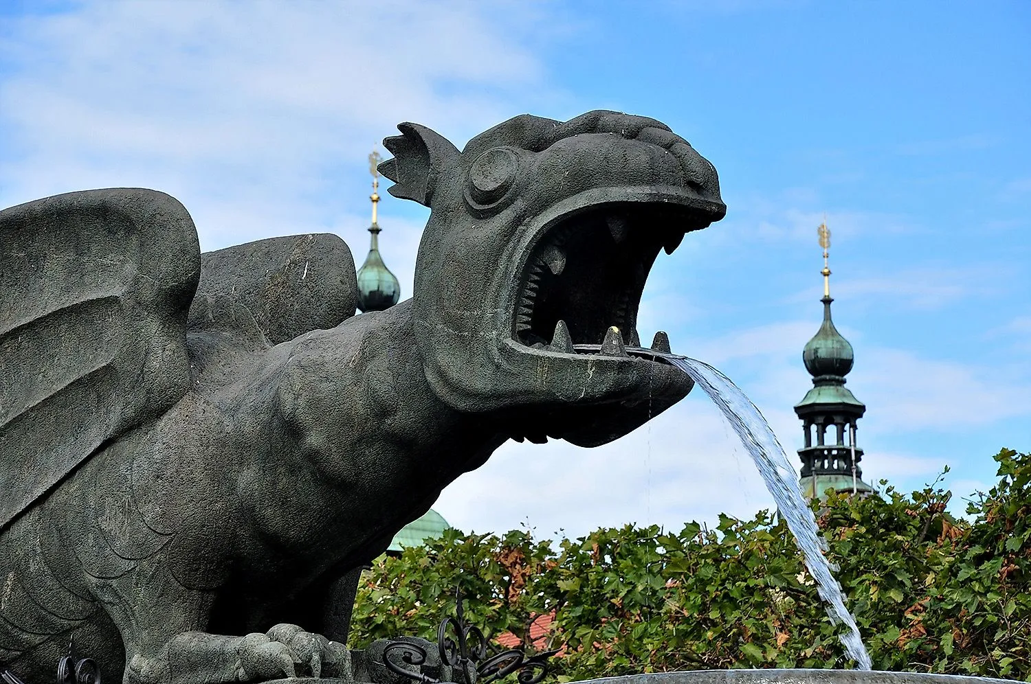 Lindwurmbrunnen in Klagenfurt mit Wasserstrahl und Türmen im Hintergrund