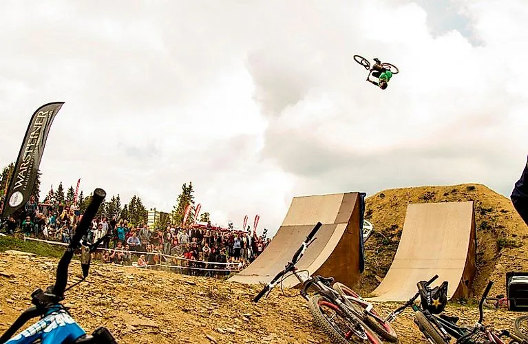 Mountain biker jumps spectacularly over ramp in front of audience at event in the Bike Arena Sauerland in Winterberg