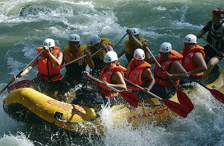 Skupinový rafting na rozbúrenej rieke vo Flachau v lete s prilbami a záchrannými vestami.