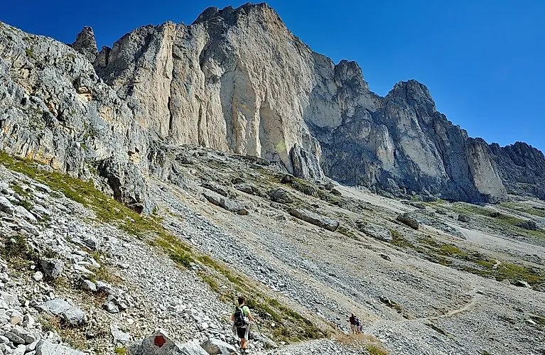 Turisti pod impozantnými skalnými stenami v Carezze v Dolomitoch za nádherného letného počasia