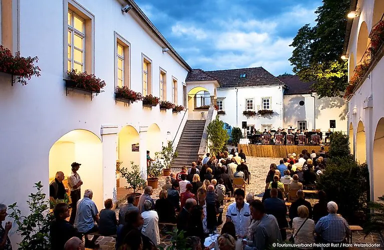 Besucherinnen und Besucher genießen ein Konzert in einem stimmungsvoll beleuchteten historischen Innenhof in Rust.