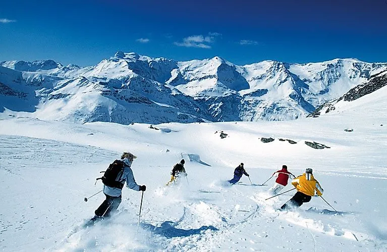 Lyžaři lyžují na čerstvém prašanu v údolí Gastein, obklopeni zasněženými vrcholky Vysokých Taur.
