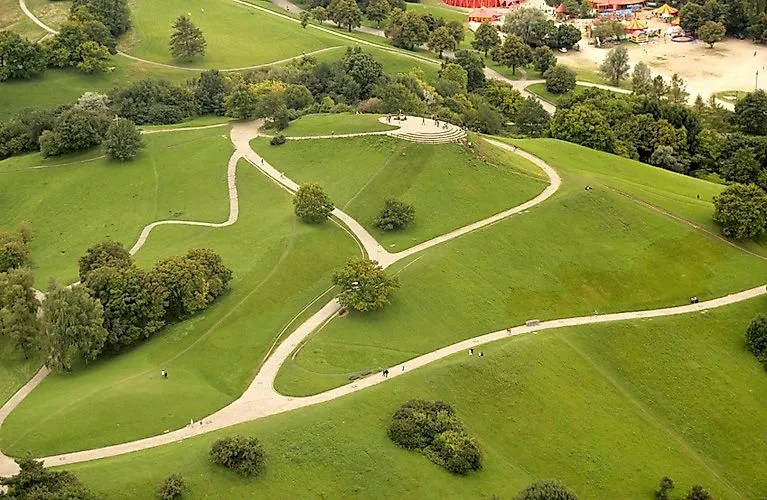 Aerial view of the English Garden in Munich with winding paths, rolling hills and scattered trees on a sunny day.