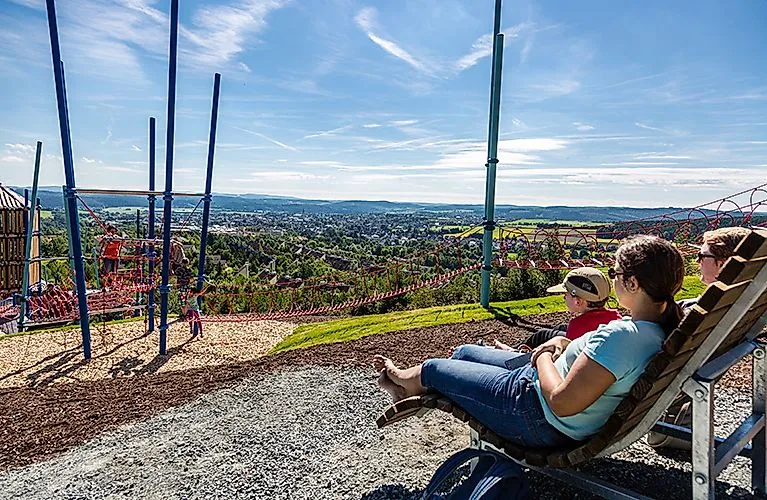 Familien genießen die Aussicht vom AVENTURA-SpielBerg in Medebach auf die umliegende Landschaft mit Spielplatz im Vordergrund.