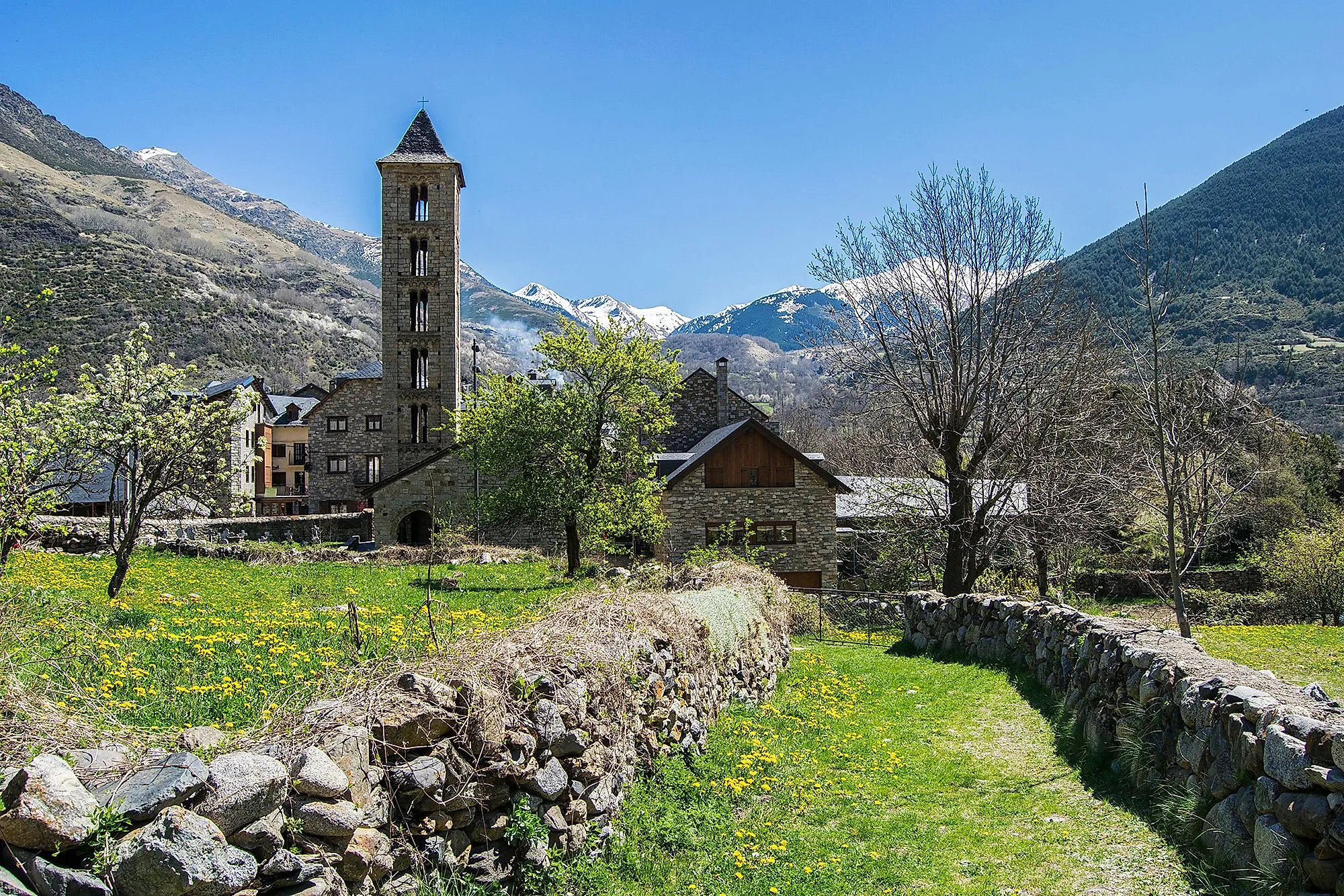 Église en pierre dans une prairie verdoyante de la Vall de Boí avec les sommets des Pyrénées en arrière-plan