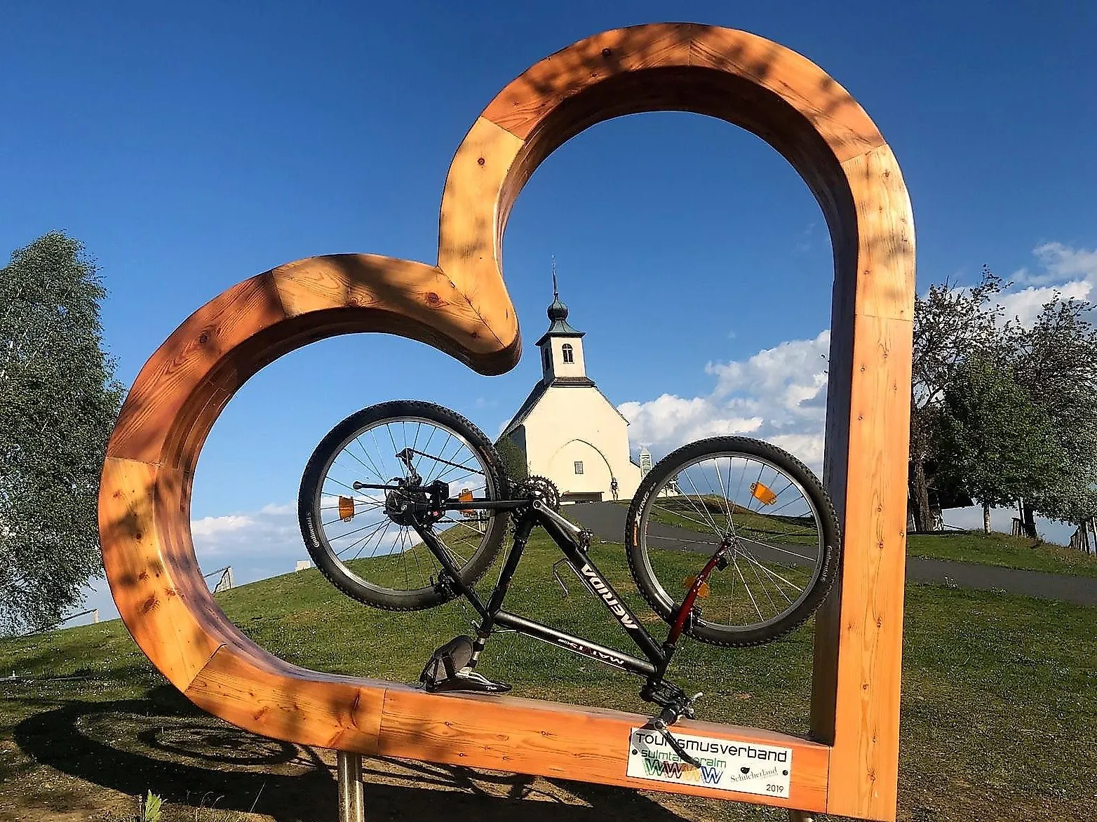 Heart-shaped wooden frame with bicycle in front of the Wolfgangi church near Bad Schwanberg