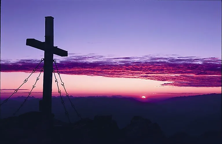 Vrcholový kríž pri východe slnka v Tirolských Alpách s veľkolepou hrou farieb na oblohe