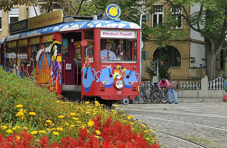 Colorful streetcar of the Ebbelwei-Express in Frankfurt with cheerful painting, in the foreground blooming summer flowers.