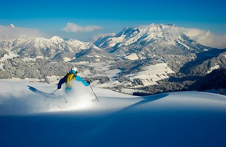 Los freeriders cabalgan por nieve polvo profunda con vistas al paisaje montañoso nevado de Fieberbrunn.