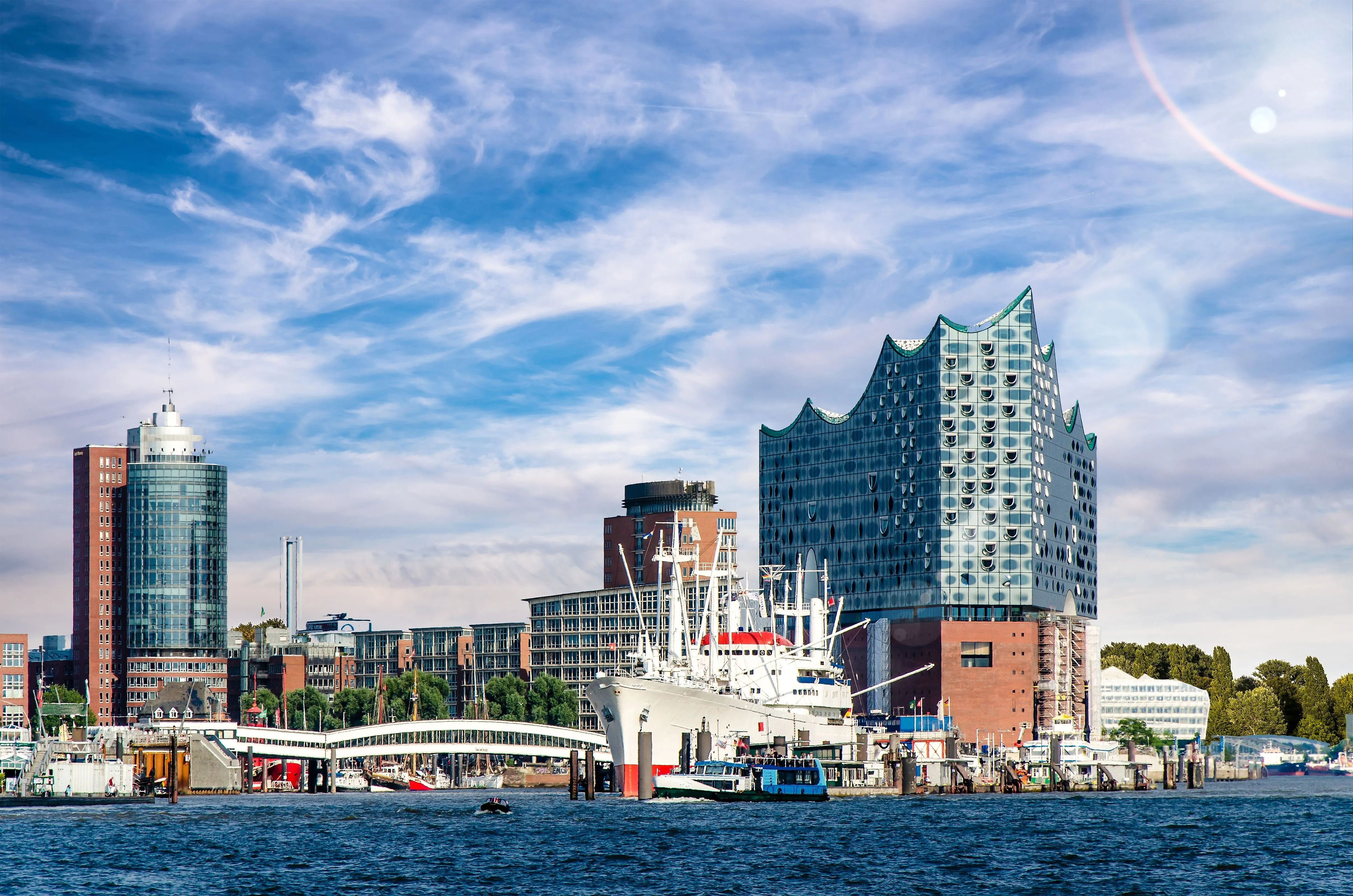 Panoramic view of the port of Hamburg with the modern Elbphilharmonie concert hall and the museum ship Cap San Diego against a blue sky.