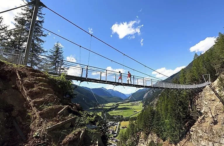 Dva turisté překračují úzký visutý most s výhledem na údolí Ötztal u Längenfeldu.