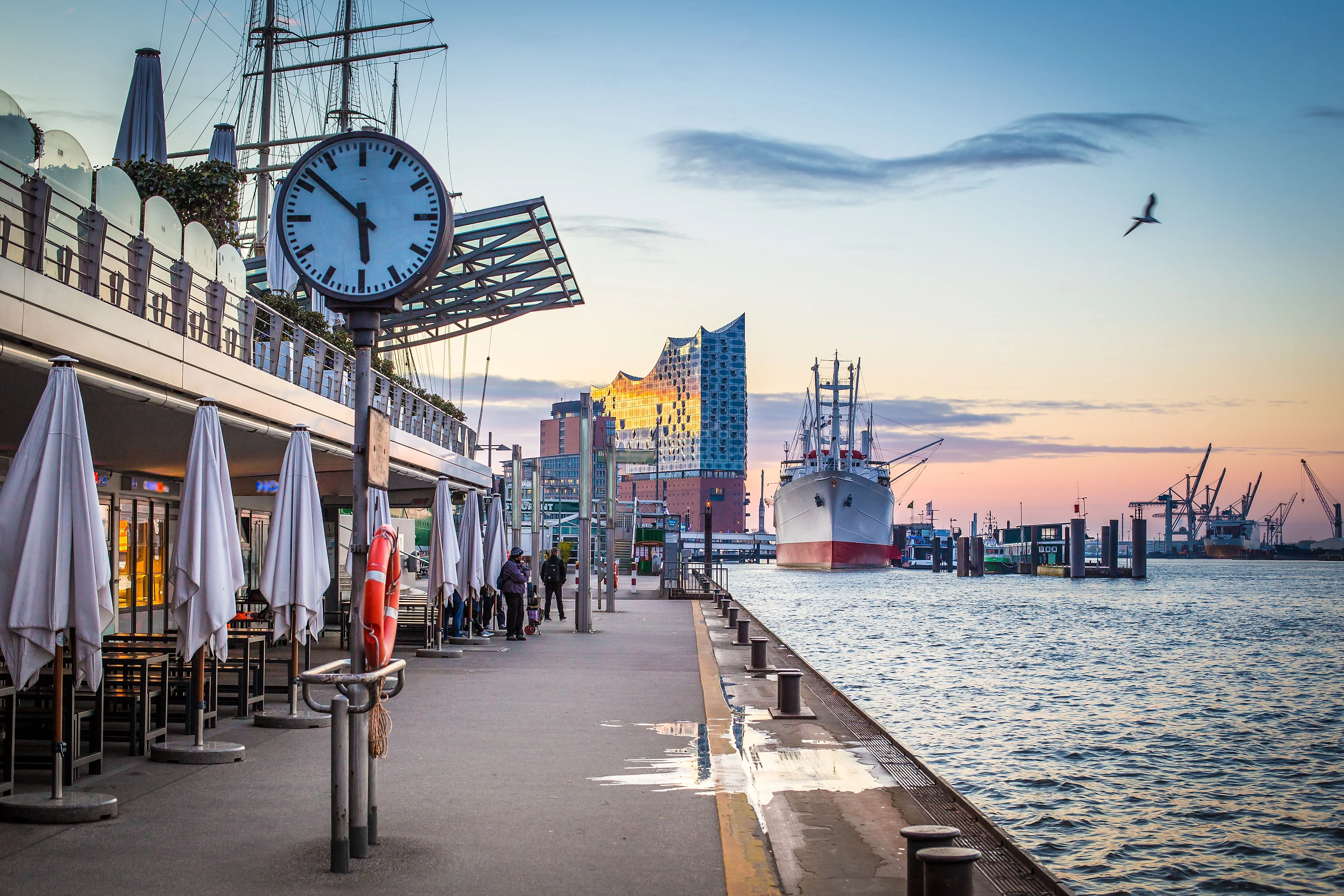 Walk along Hamburg's Landungsbrücken with a view of the museum ship Cap San Diego and the illuminated Elbphilharmonie at sunset.