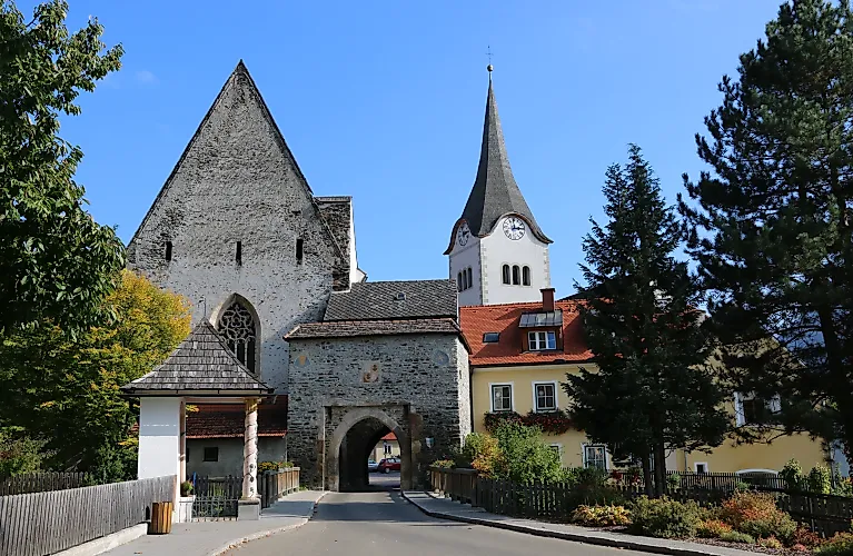 Středověký Hintereggertor s kostelem a barevnými domy v Oberwölzu za slunečného letního dne.