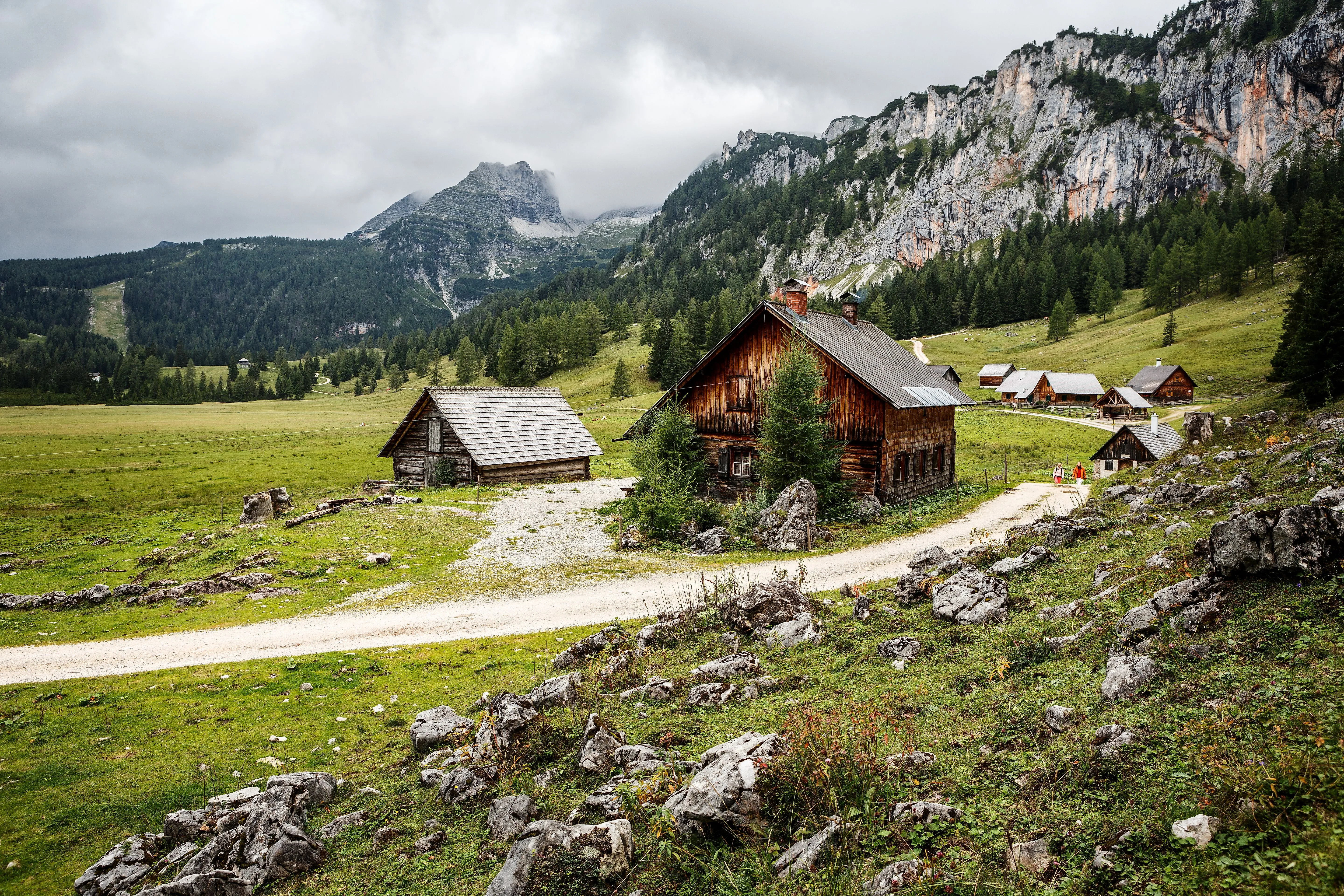 Traditional alpine huts on the Wurzeralm near Hinterstoder in the middle of a green mountain landscape with a cloudy sky.