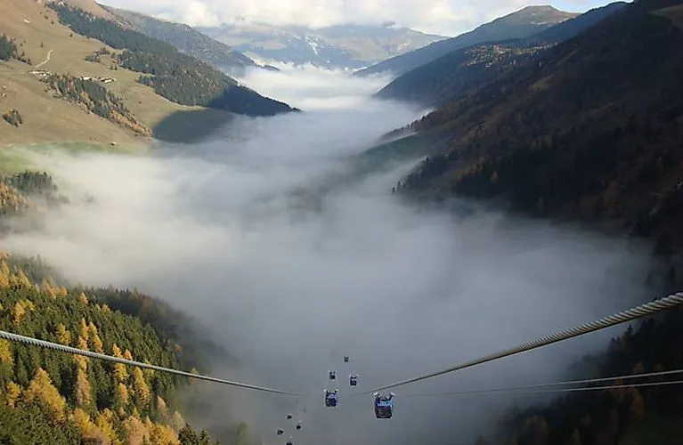 Blick aus der Seilbahn auf das mit Nebel gefüllte Tal bei Hintertux in Tirol, umgeben von herbstlich gefärbten Hängen und Alpengipfeln.