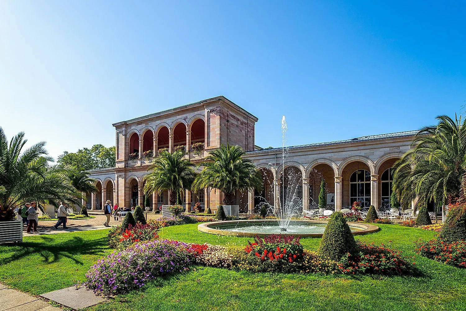 Lázeňské zahrady Bad Kissingen s Wandelhalle, palmami a fontánou na slunci