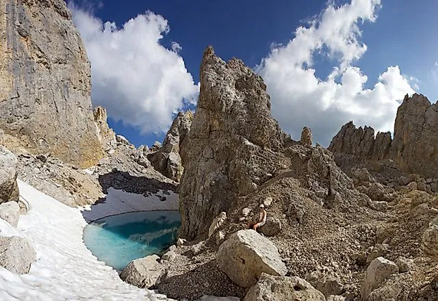 Lago glaciale vicino a Obereggen con lago blu turchese tra rocce e resti di neve nel massiccio del Latemar