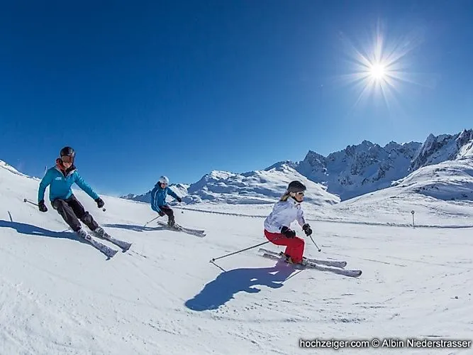 Three skiers on a perfectly groomed piste on the Hochzeiger in the Pitztal valley under a glorious winter sun.