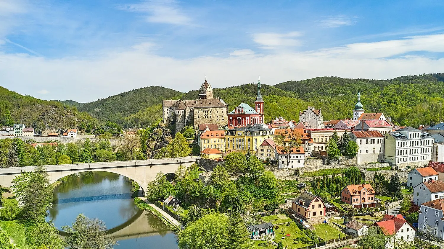 Pohľad na stredoveký hrad Loket a farebné staré mesto obklopené zeleňou pri Karlových Varoch