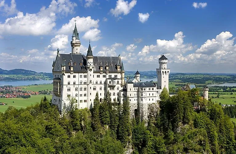 Märchenschloss Neuschwanstein vor Alpenkulisse, eingebettet in grüne Wälder und weite Landschaft.