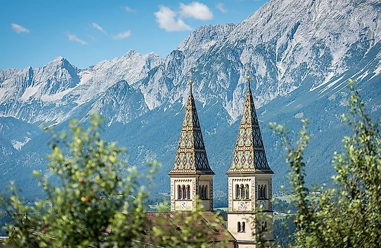 Dos ornamentadas agujas de iglesia se elevan hacia el cielo frente a las montañas de Karwendel con tiempo despejado en verano.