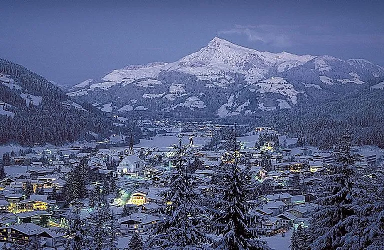 Verschneites Kirchberg in Tirol in der Dämmerung mit Lichtern der Häuser und dem verschneiten Gaisberg im Hintergrund.