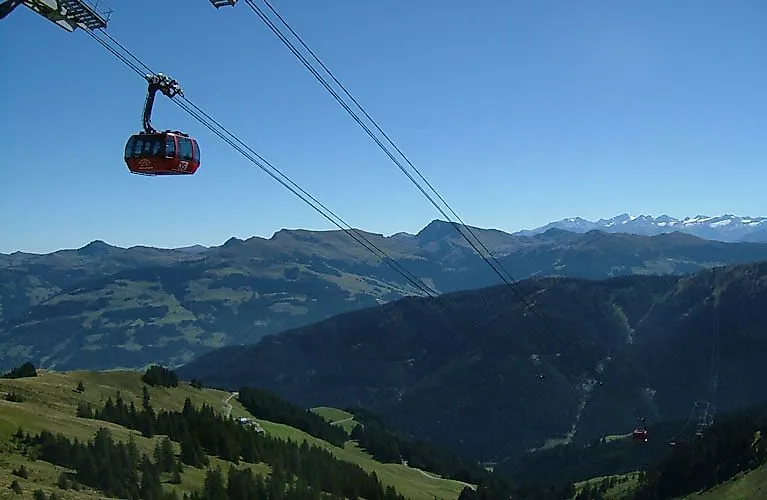 The red cable car gondola floats above the mountain slopes of Kirchberg with a wide view of the Kitzbühel Alps.