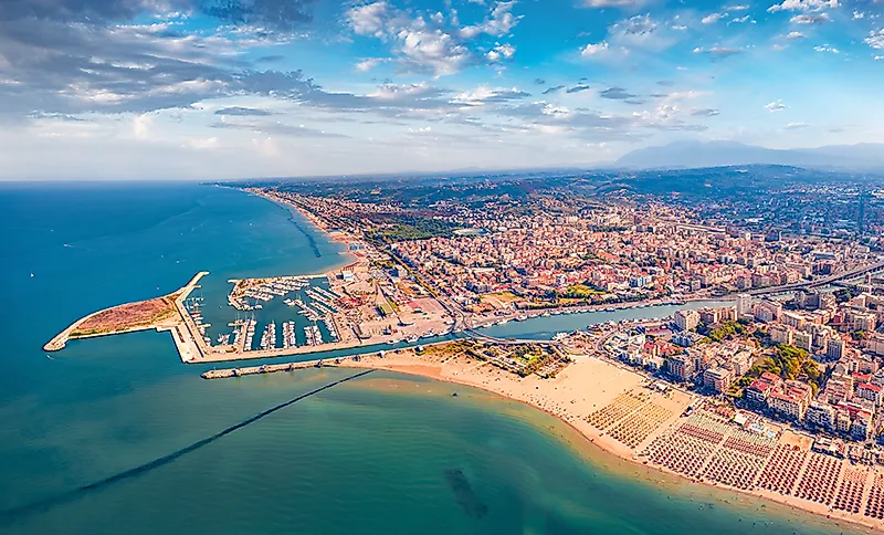 Kustplaats met haven, strand en dichtbebouwd gebied aan een lang zandstrand onder een blauwe hemel