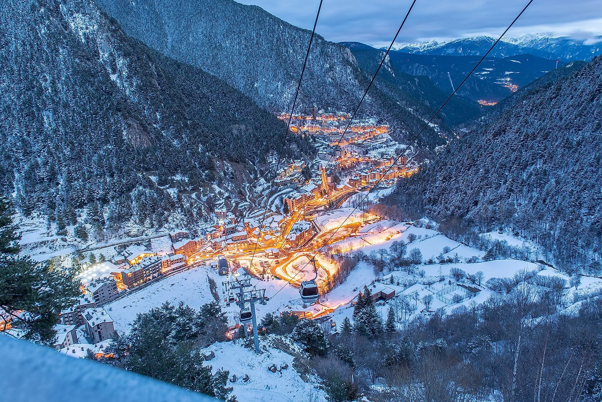 Zasněžený Arinsal v Andoře s osvětlenými ulicemi a lanovkou v zimním večeru