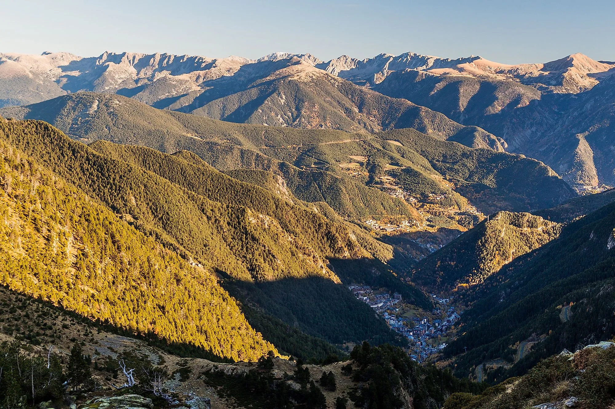 Pohled z ptačí perspektivy na zelené horské svahy a vesnici Arinsal v Andoře za jasného letního dne