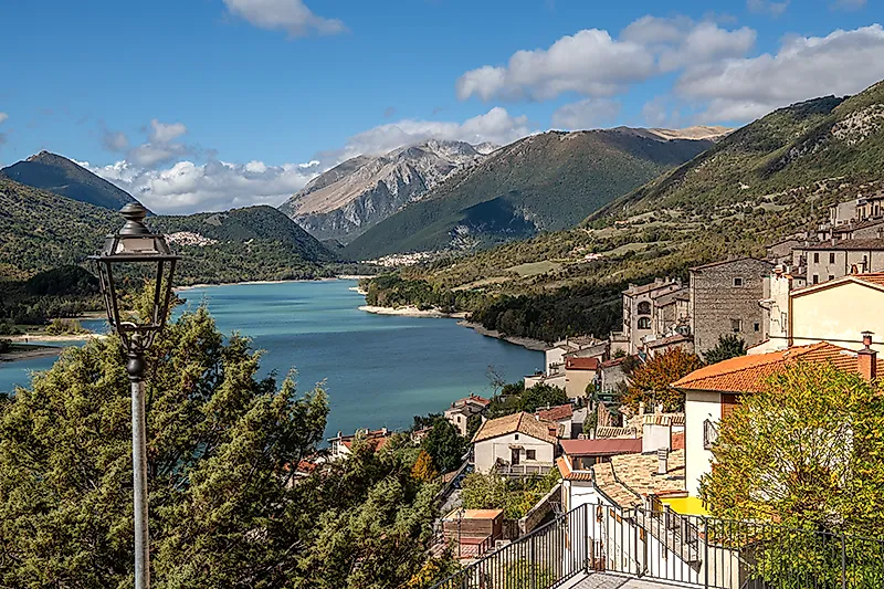 Bergdorp met meer in een alpine landschap, huizen op een helling en uitzicht op bergen onder een blauwe hemel