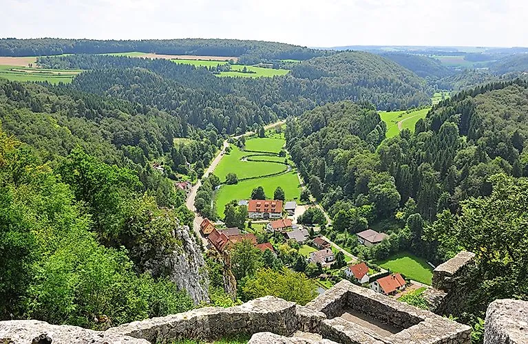 Panoramatický výhled na Lautertal se zelenými lesy, loukami a roztroušenými domy - typická krajina Švábského Albu