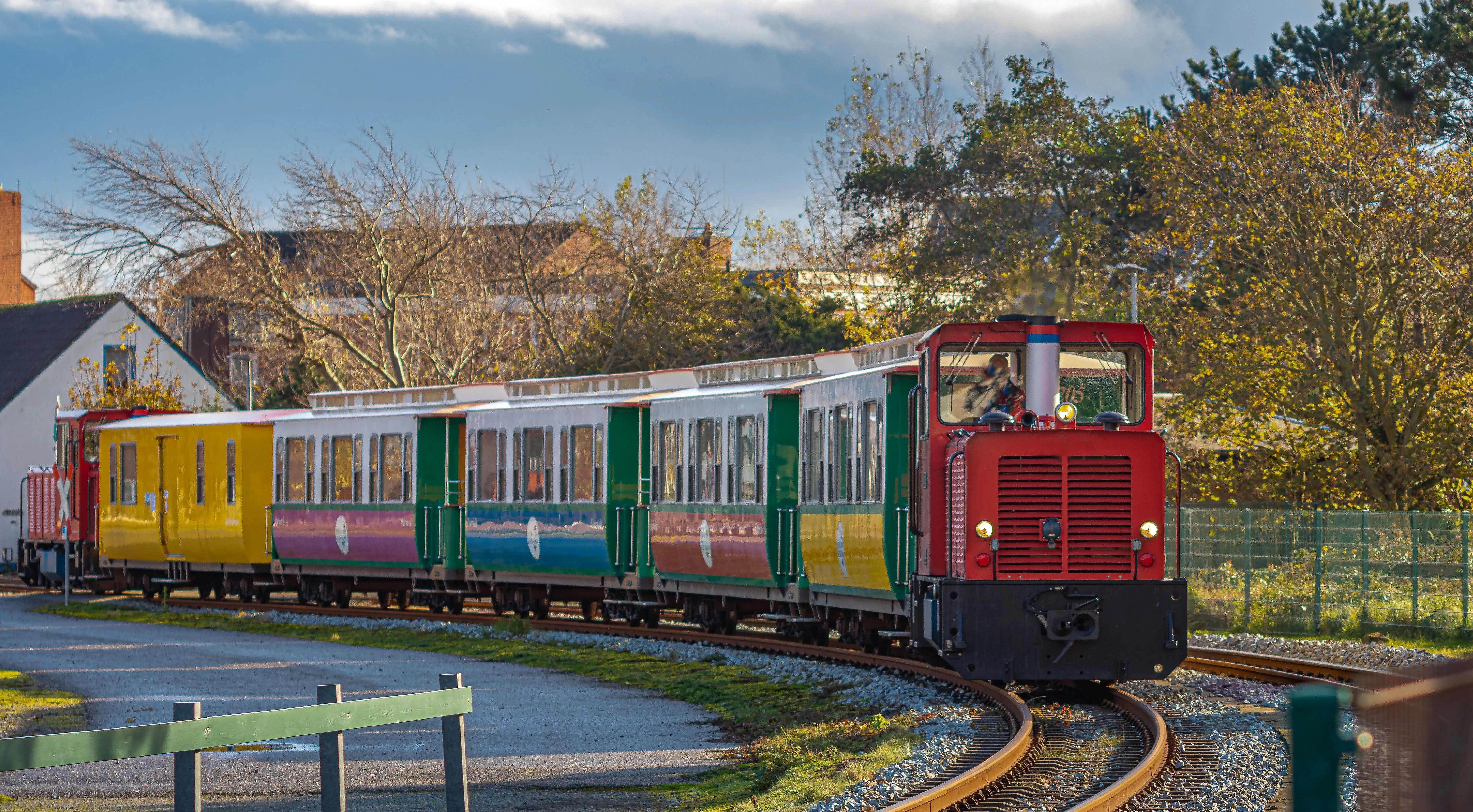 Colorful island railroad on Borkum runs through autumnal landscape with historic carriages.