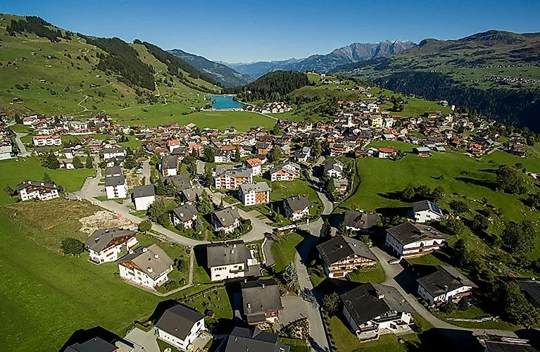 Vue aérienne de Brigels en Suisse en été, avec vue sur les montagnes environnantes et les prairies verdoyantes.