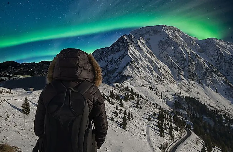 grüne Polarlichter am Nachthimmel über verschneiter Berglandschaft in Grönland