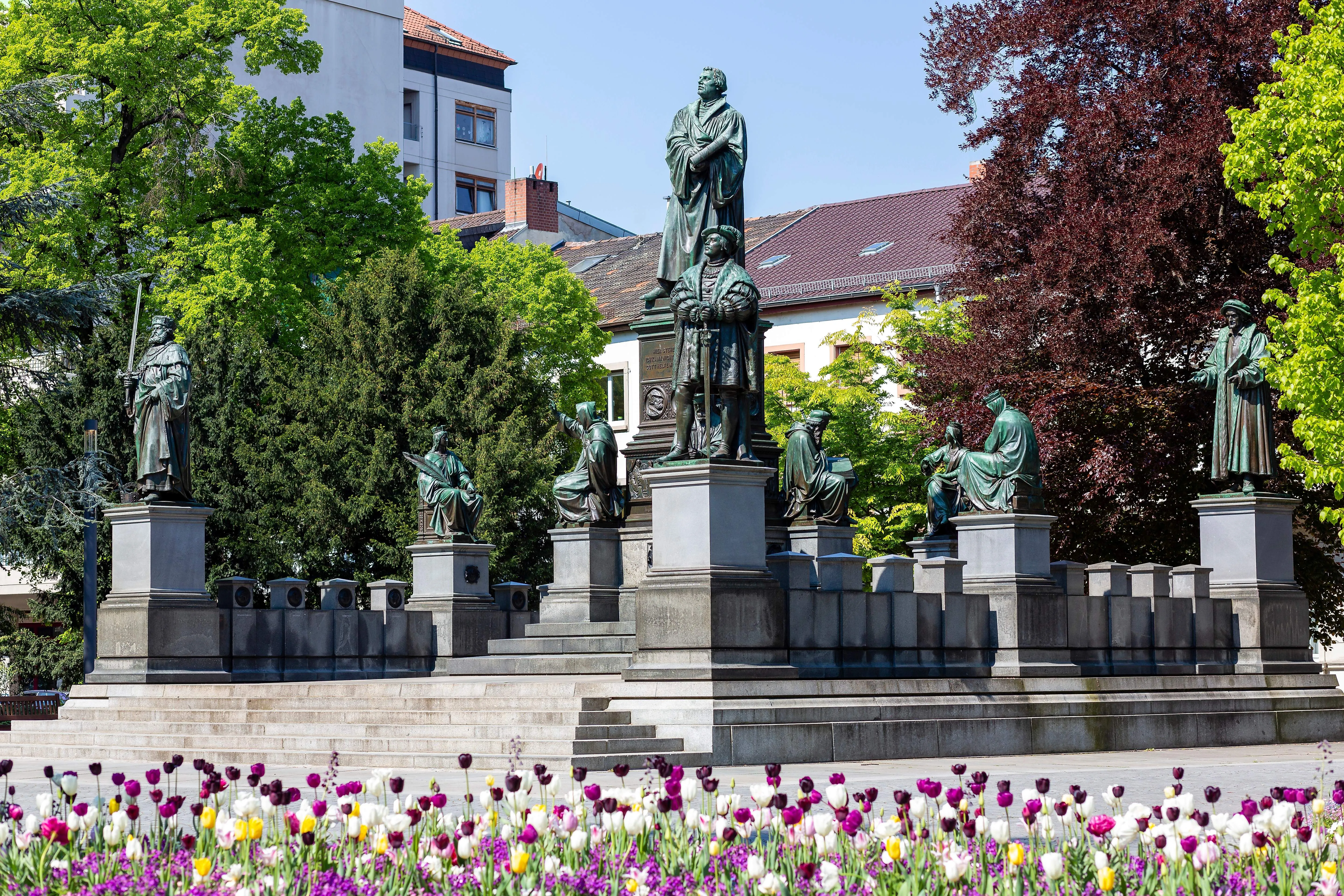 Het Martin Luther monument in Worms met omringende beelden en bloeiende tulpen.