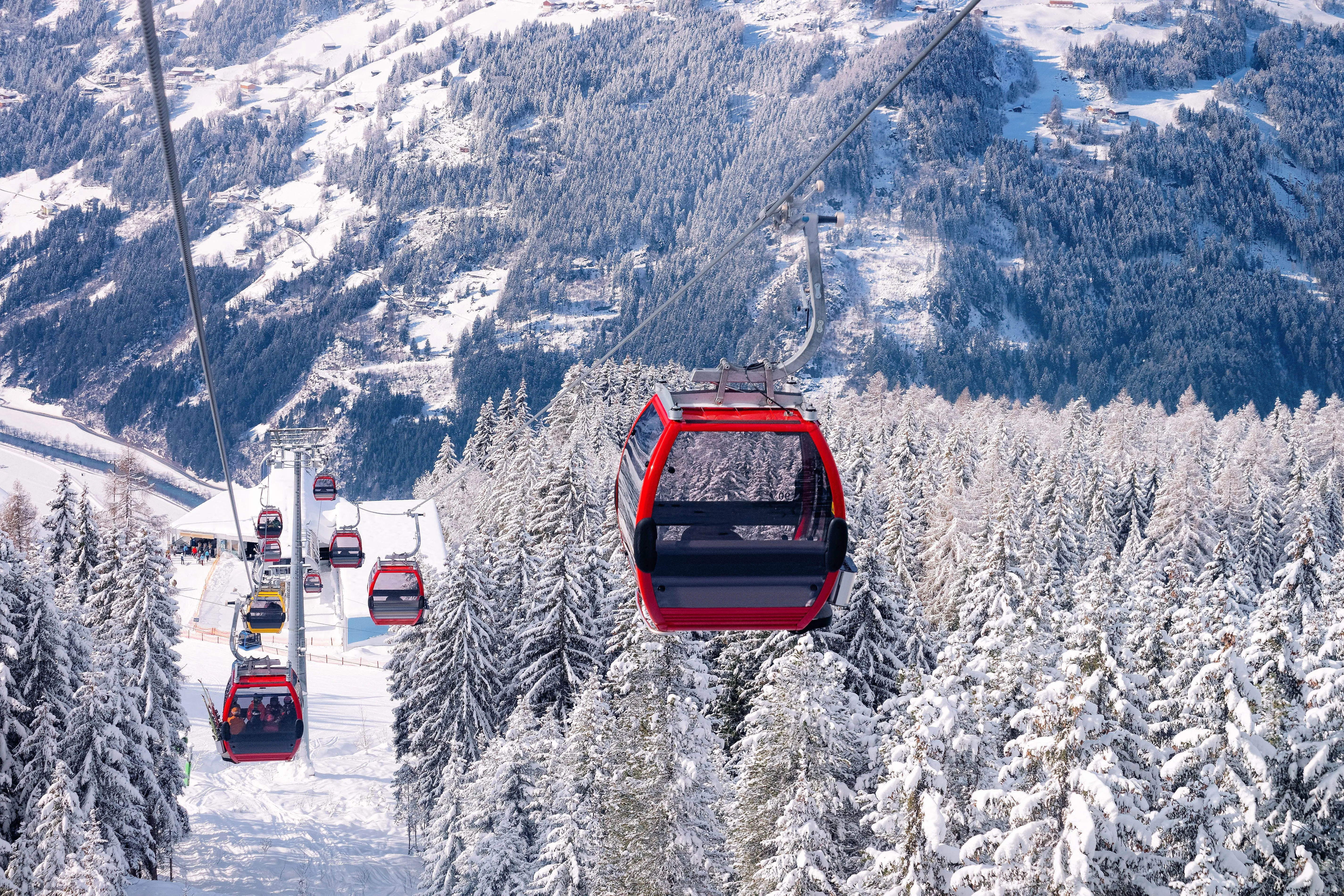 Red gondola lift rides through snow-covered coniferous forest in Mayrhofen in the Zillertal, Tyrol.
