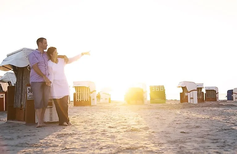 Couple standing barefoot between beach chairs on Norddeich beach before sunset.