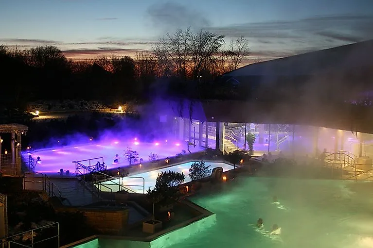 Atmosféricky osvětlený venkovní bazén v PanoramaTherme Beuren v noci se stoupající párou
