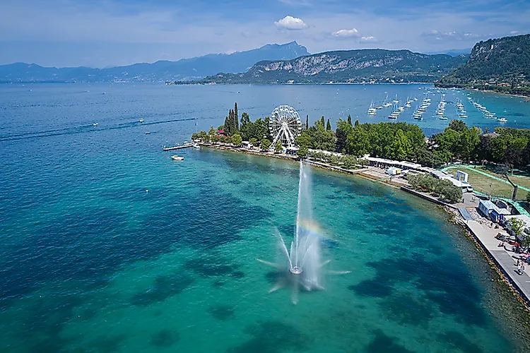 Halbinsel am Gardasee bei Lazise mit Springbrunnen, Riesenrad und Yachthafen vor Bergkulisse