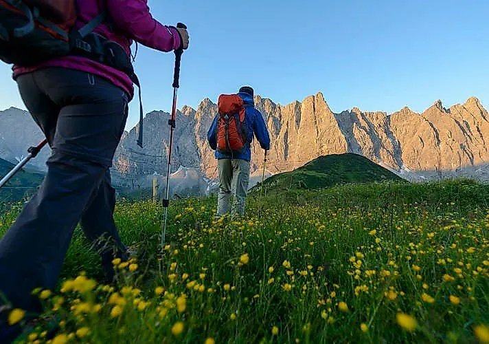 Senderistas a primera hora de la mañana en un prado en flor con vistas a las impresionantes montañas Karwendel, cerca de Schwaz.