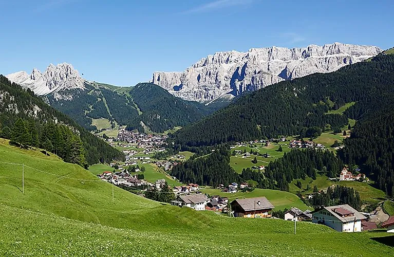 Selva di Val Gardena in summer with green meadows and the Dolomites in the background
